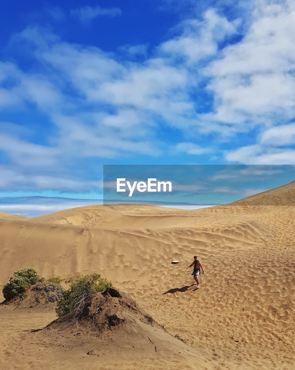 Shirtless man walking on sand in desert against sky