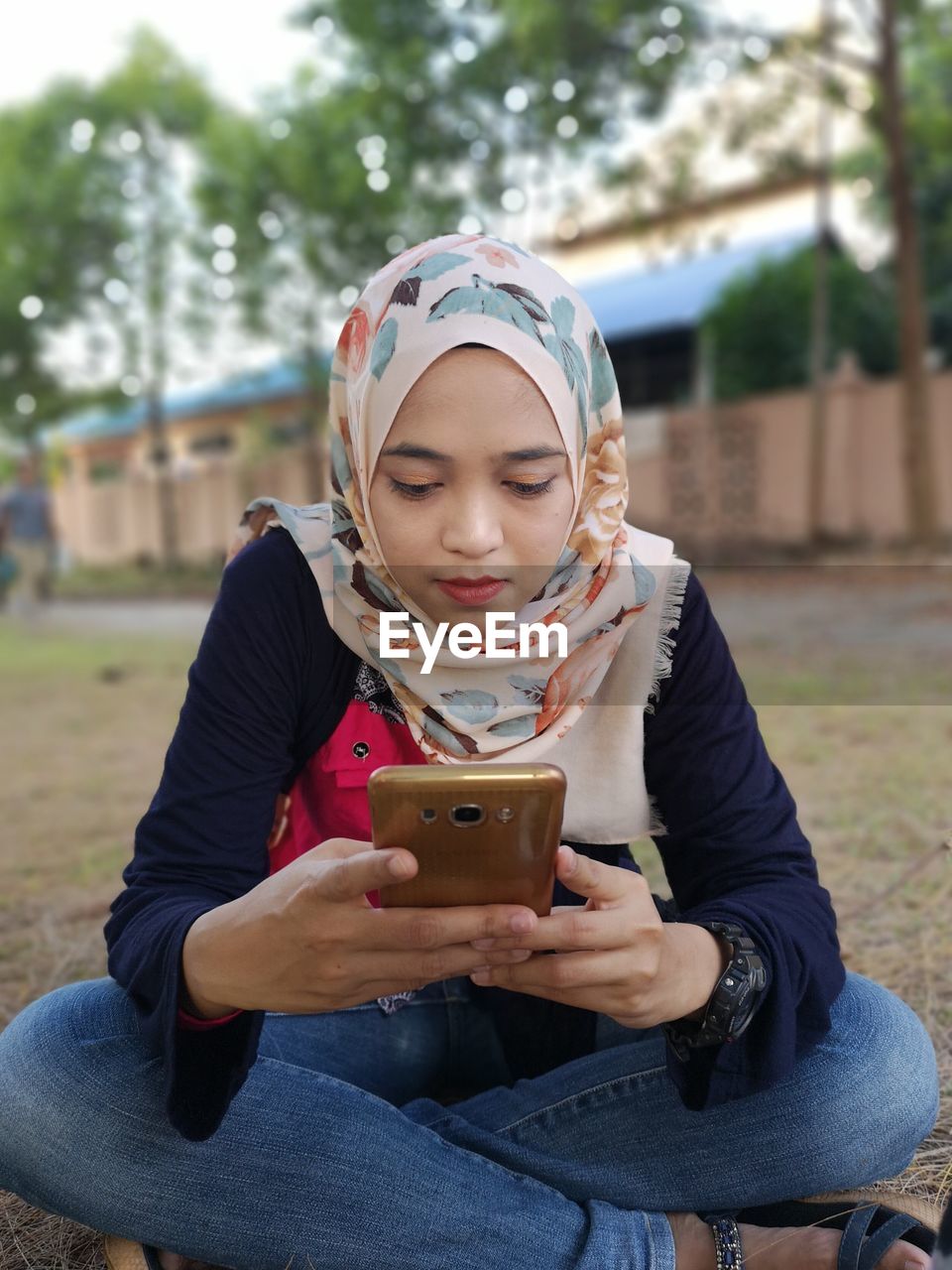 Young woman using phone while sitting on field