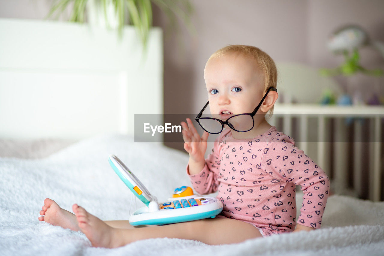 portrait of cute girl using digital tablet while sitting on bed at home