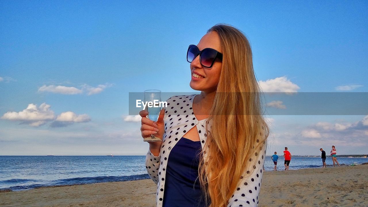 Young woman holding wineglass at sopot beach against sky
