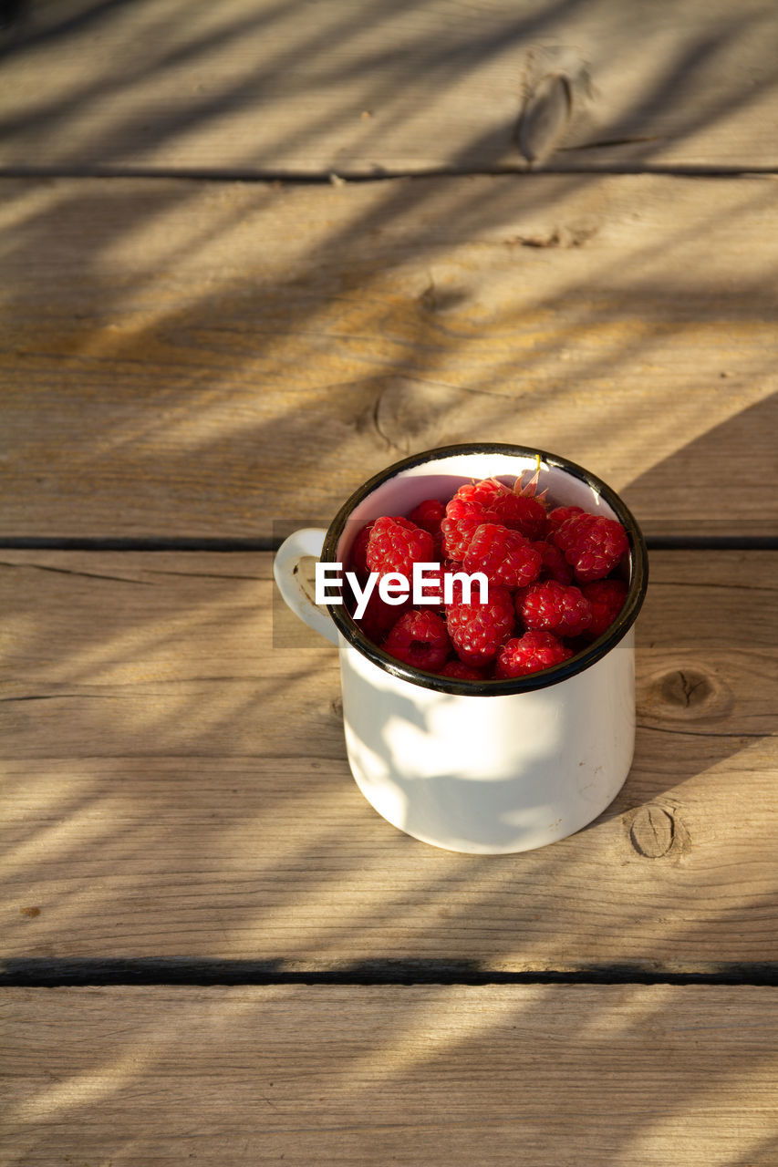 Fresh organic raspberries in white cup on wooden background