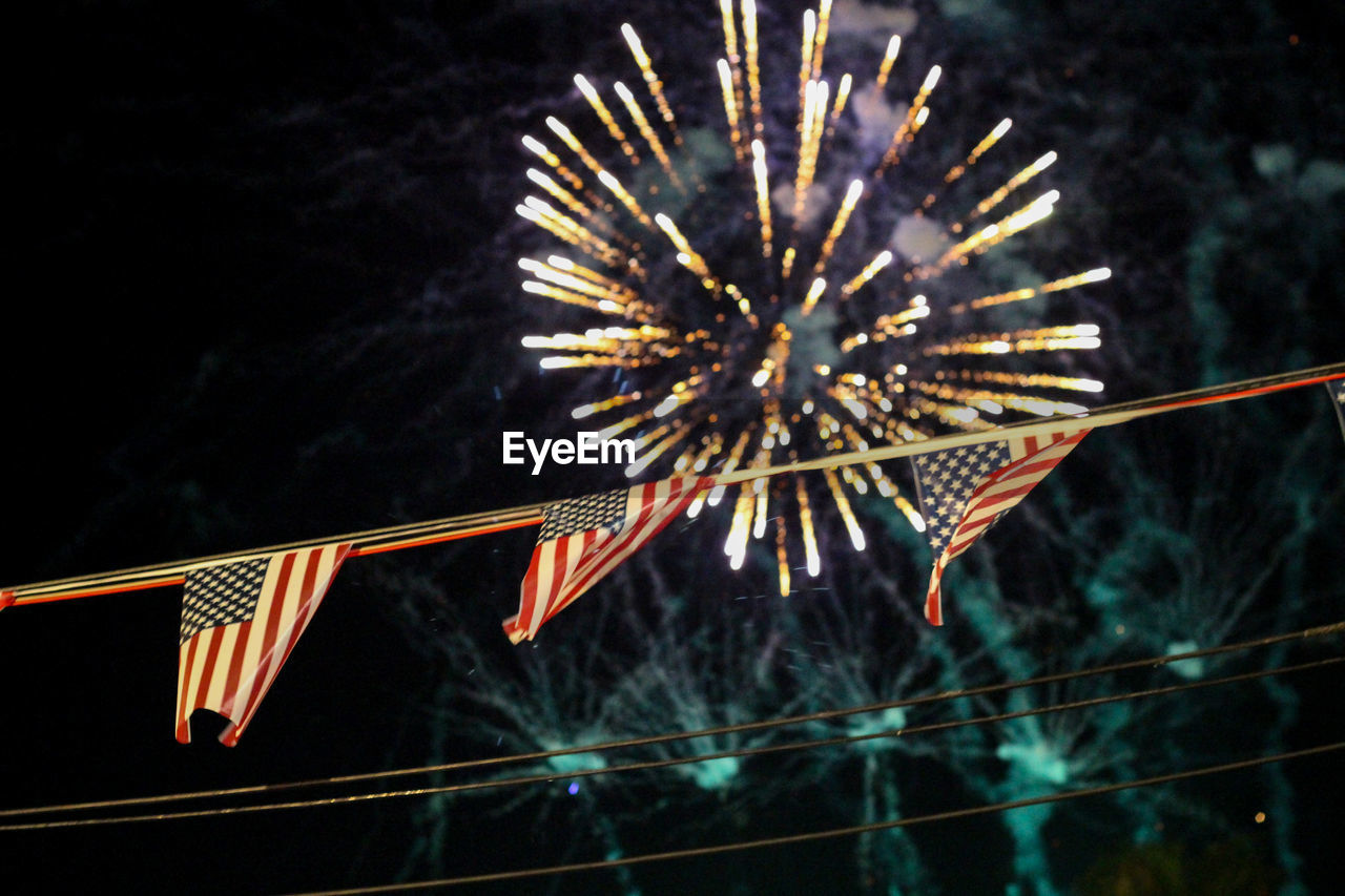 Low angle view of american flags against illuminated fireworks at night