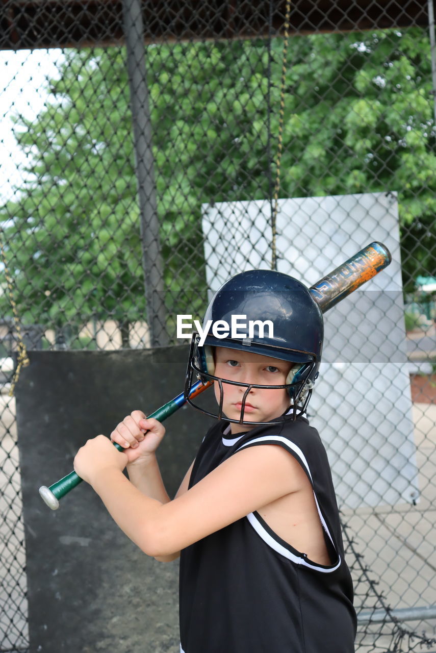 Portrait of boy holding a bat while standing by fence