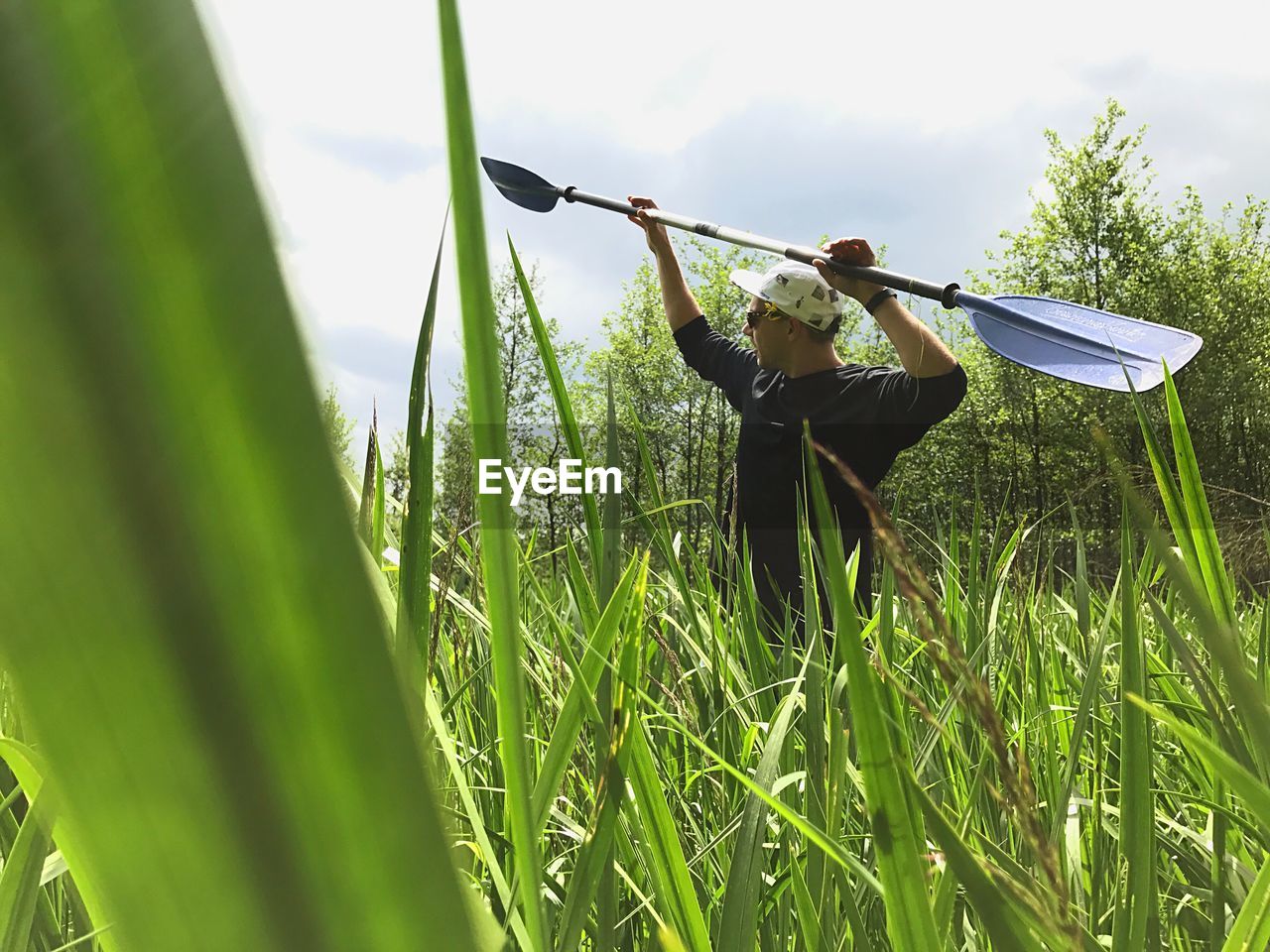 Young man holding oar while standing on grassy field during sunny day