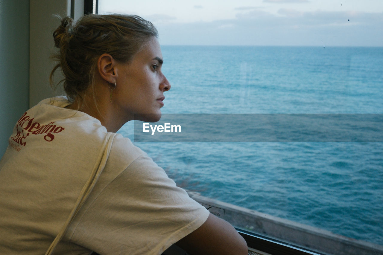 Young woman looking through window in boat against sea
