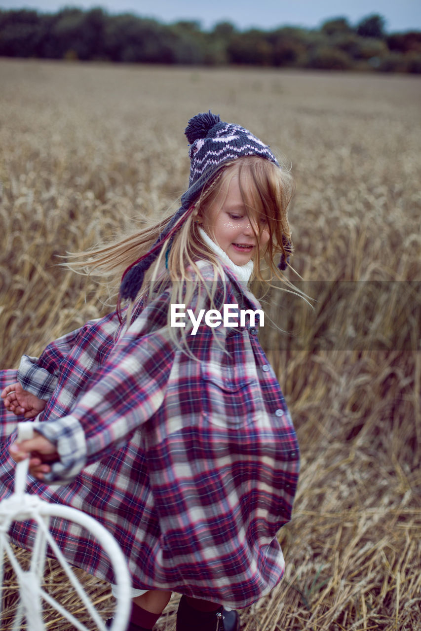 Blonde girl in white in a dress and boots goes with a dream catcher in a wheat field