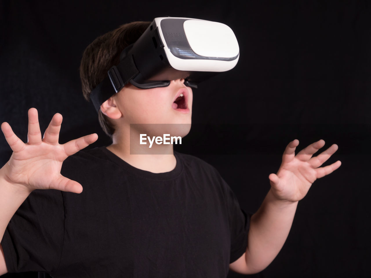 Boy gesturing while wearing virtual reality simulator against black background