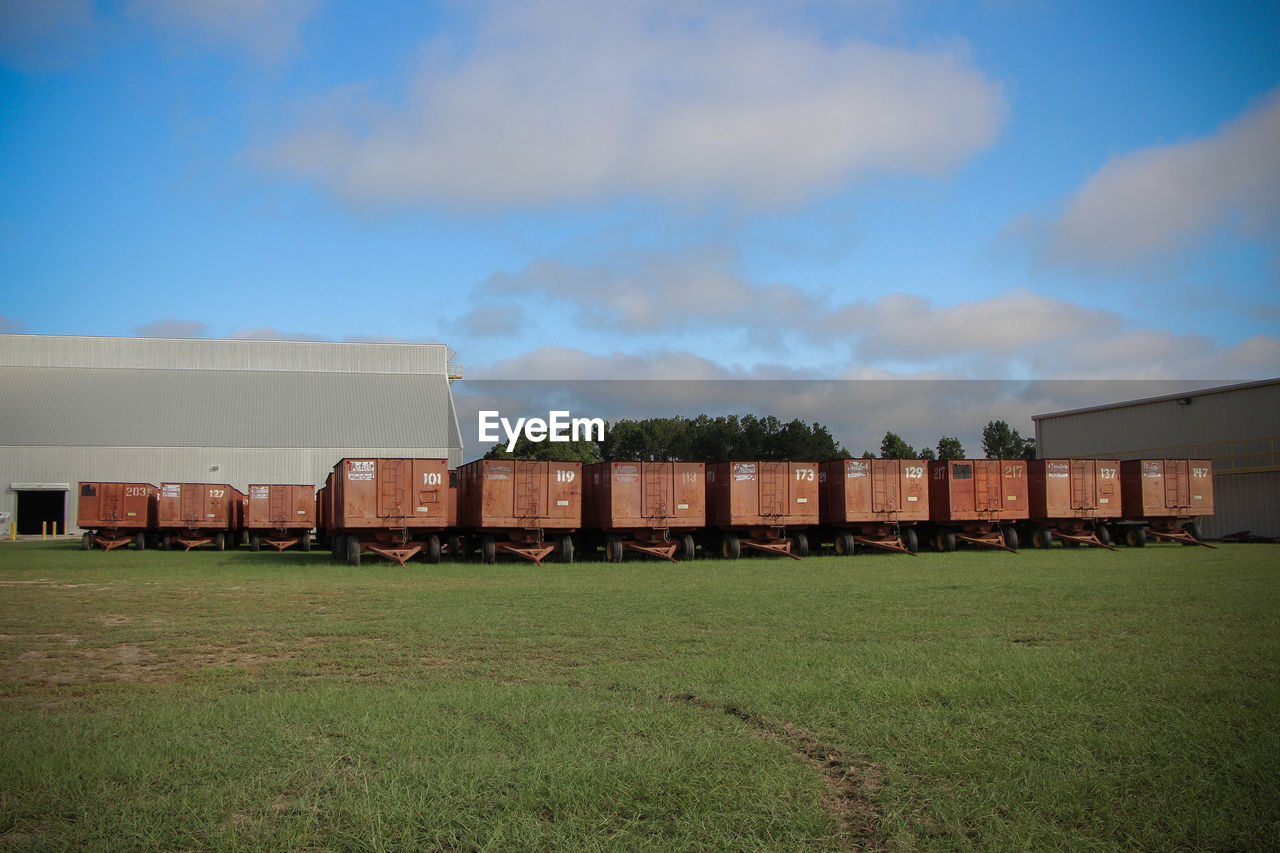 Vehicle trailers on grassy field against sky