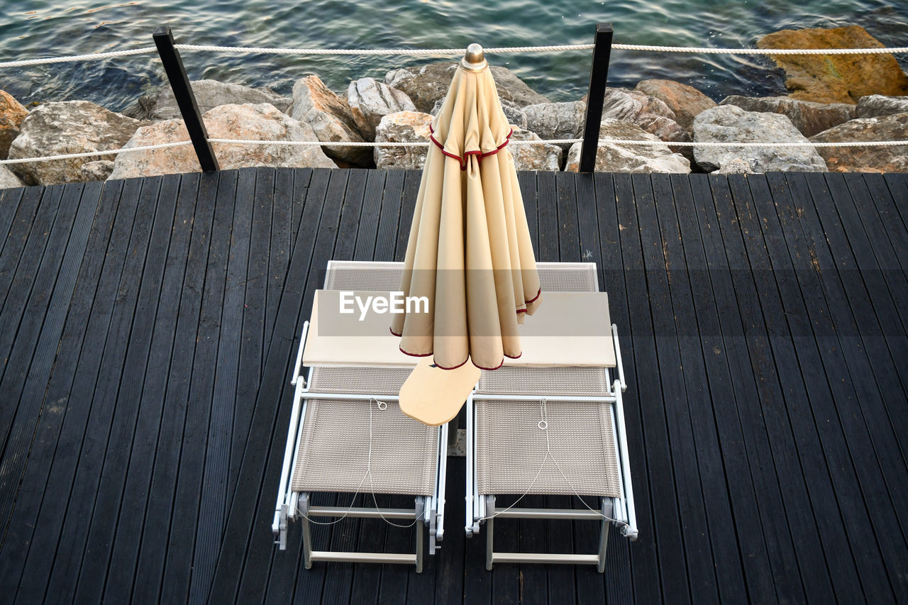 High-angle view of a pair of sunbeds under a closed beach umbrella on the seashore