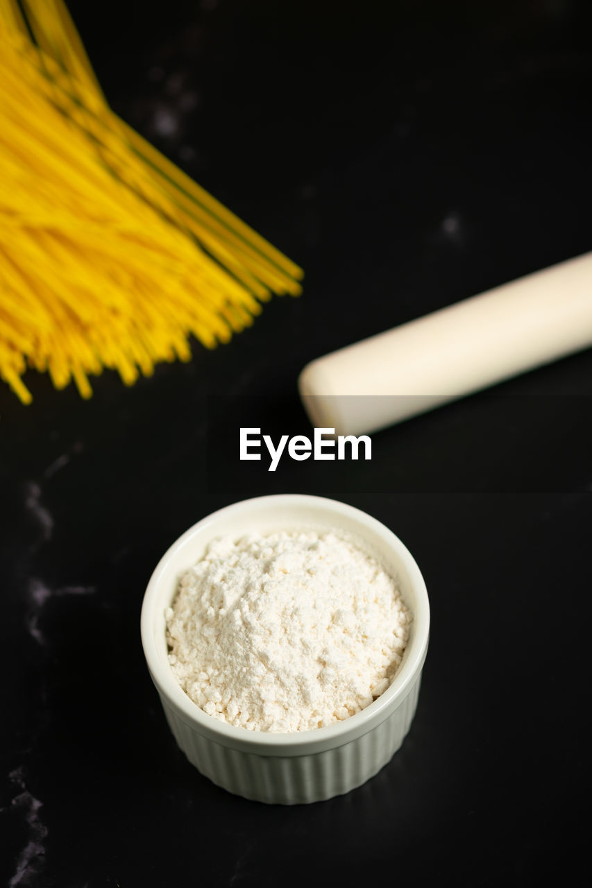 Concept of making spaghetti noodles.cup of flour.flour,rolling pin,noodles on dark background.