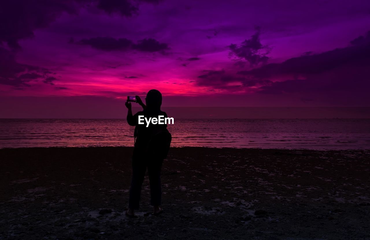 Silhouette man standing on beach against sky during sunset