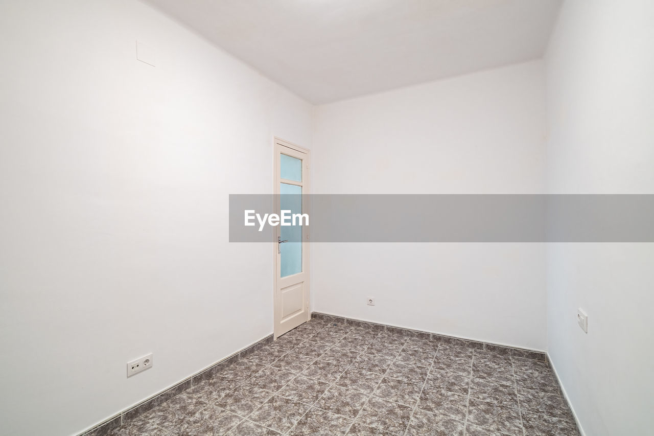 Room interior after renovation, unfurnished apartment with white walls, tiled floor and small door.