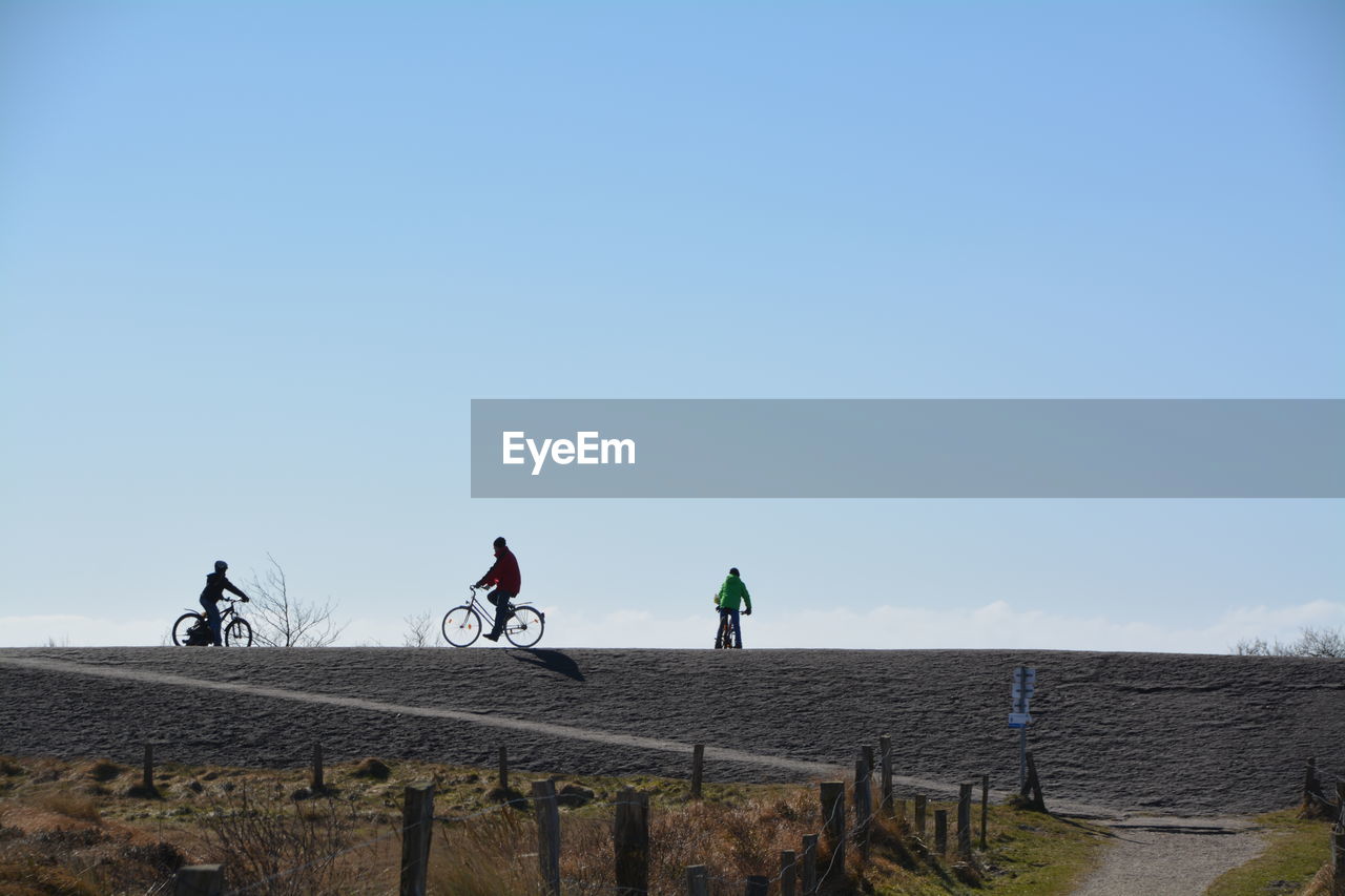 Low angle view of people riding bicycle on hill against sky