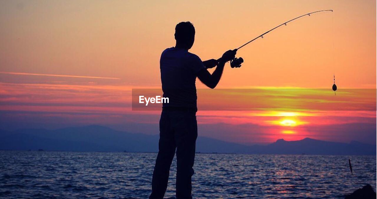 Silhouette man fishing in sea against sky during sunset