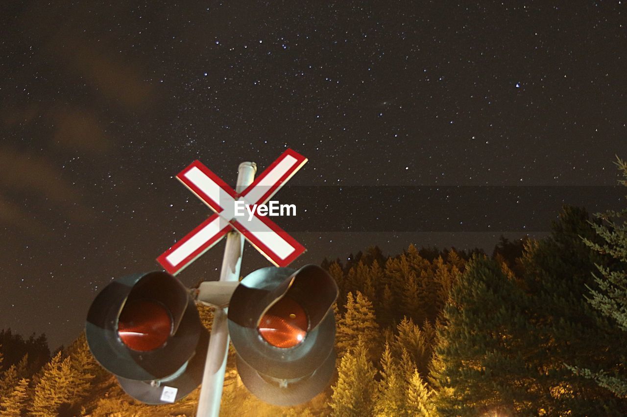 Low angle view of railroad crossing by trees against star field