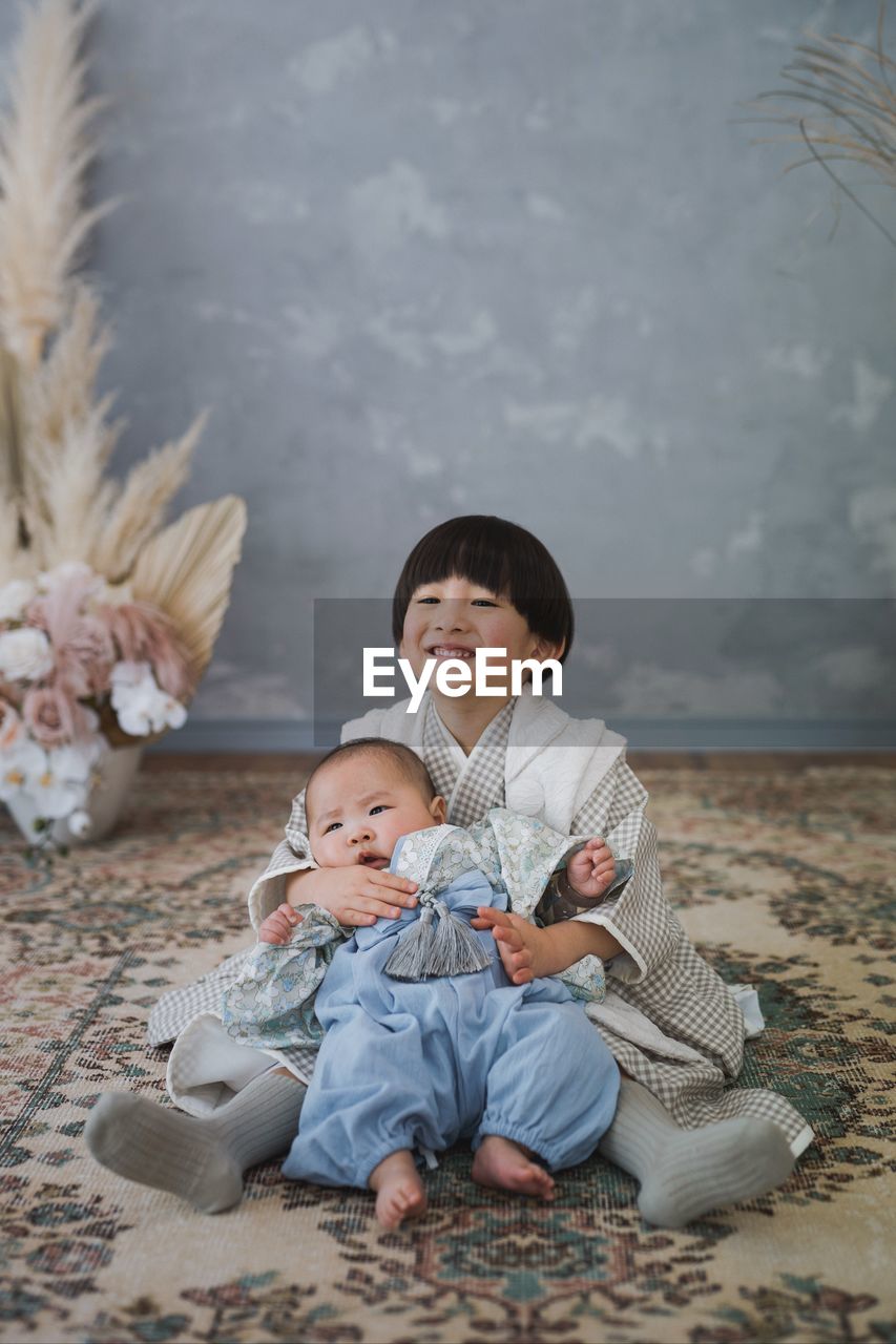 Portrait of boy and baby sitting on field. kimono