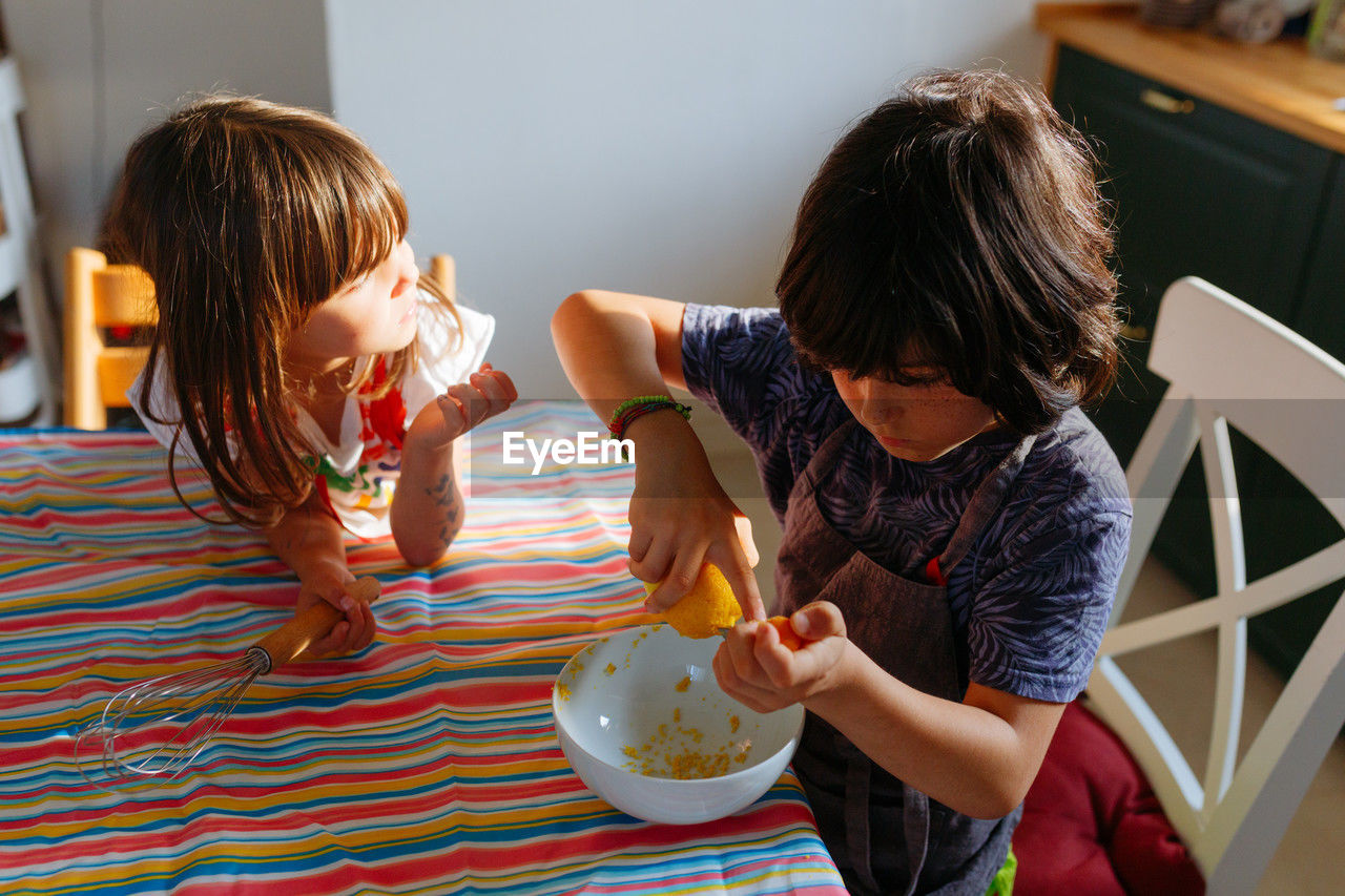 Two girls sitting at the table preparing cake in the kitchen at home