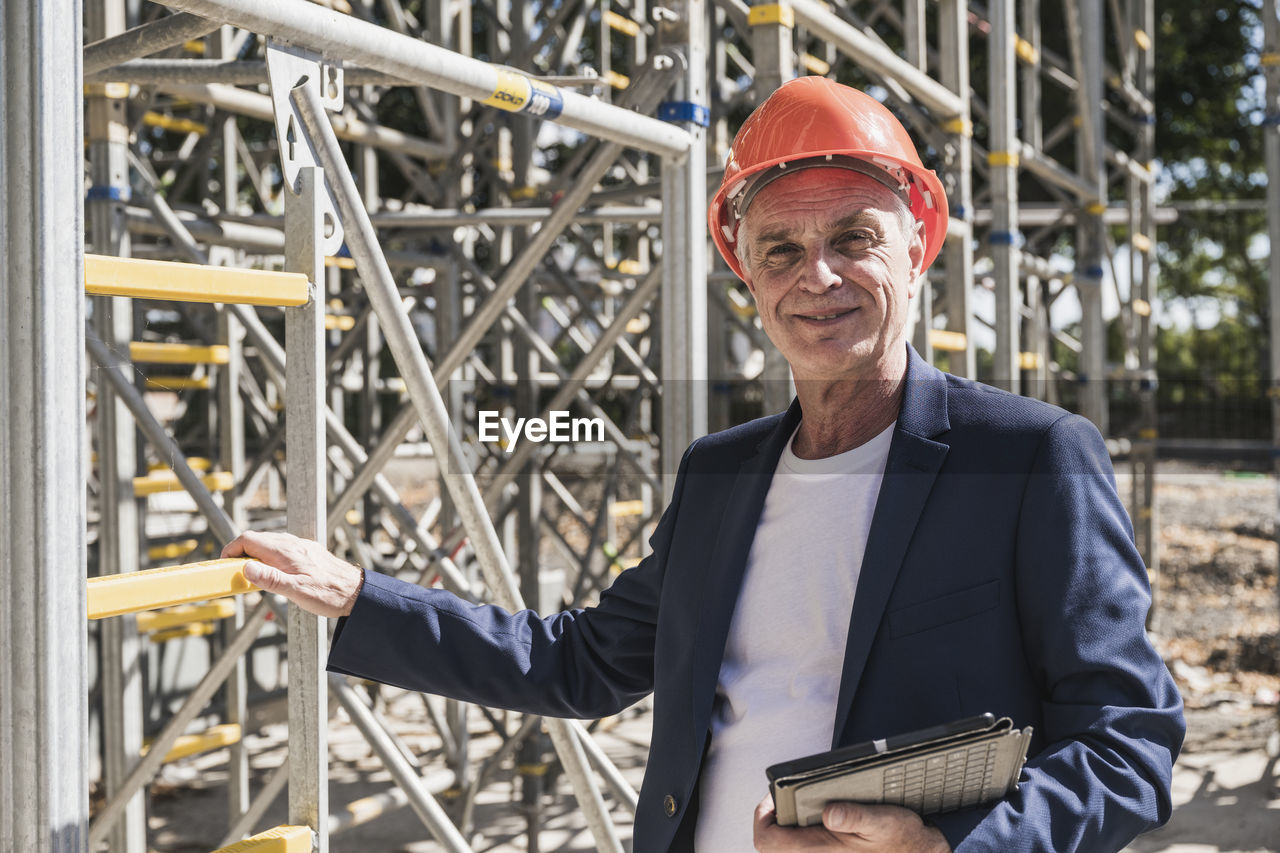 Smiling architect with tablet pc standing by scaffolding