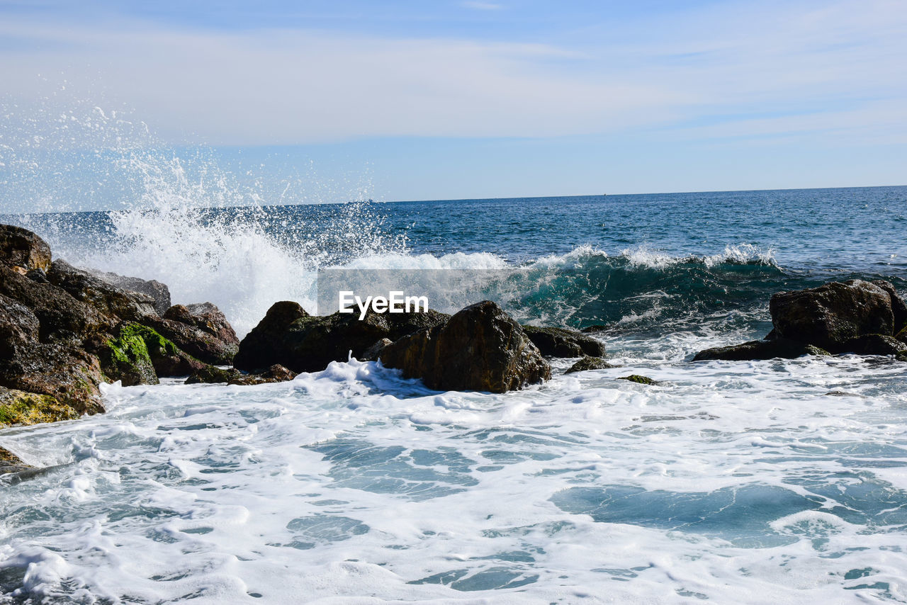 WAVES SPLASHING ON ROCKS AT SEA AGAINST SKY