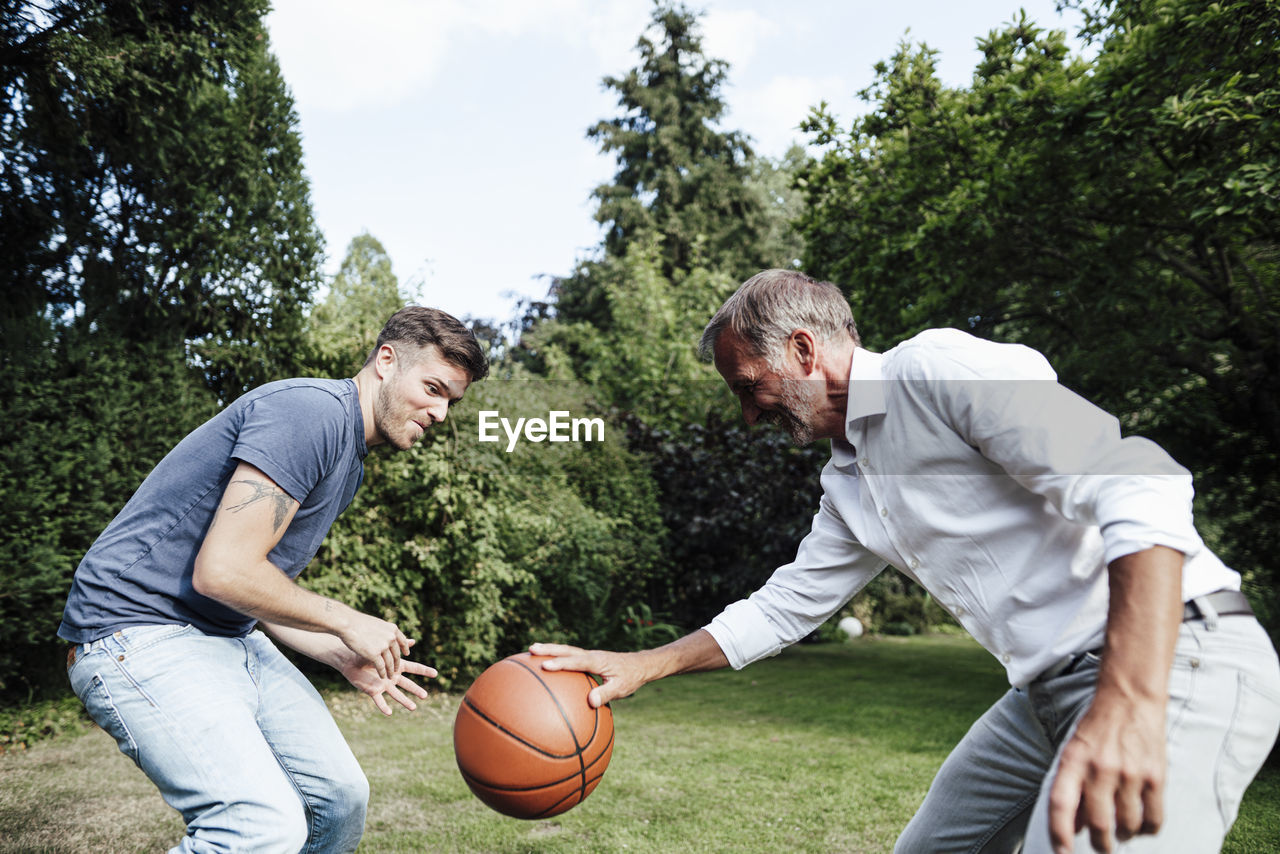 Father playing basketball with son in backyard during sunny day