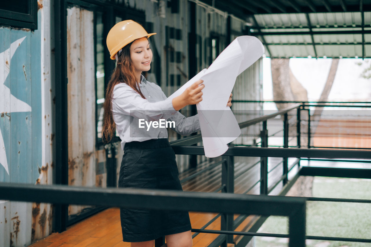 Young engineer holding blueprint while standing at site