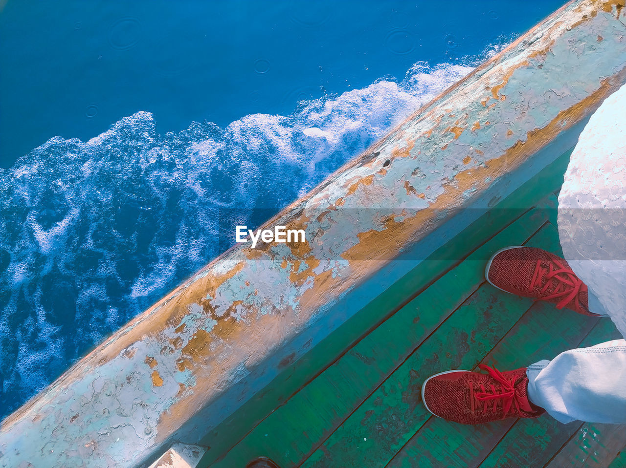 Low section of person standing on boat deck over sea