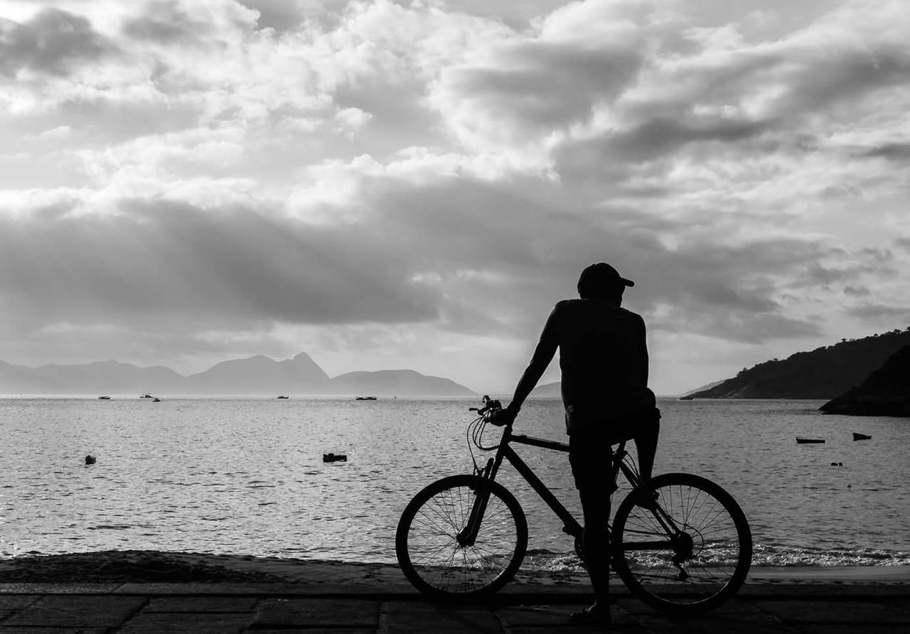 REAR VIEW OF MAN BICYCLING ON BEACH