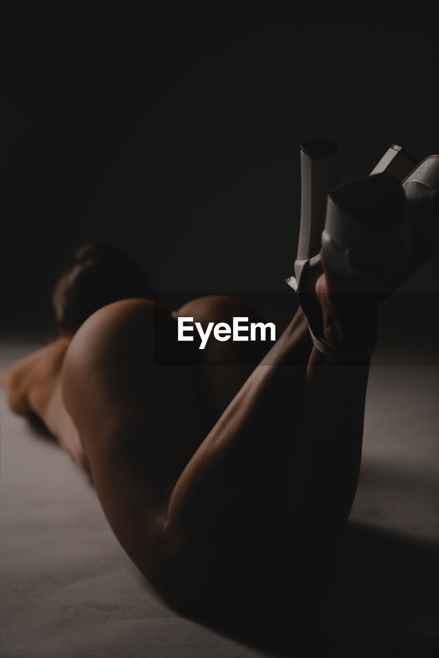 Rear view of sensuous woman kneeling on floor with high heels midair