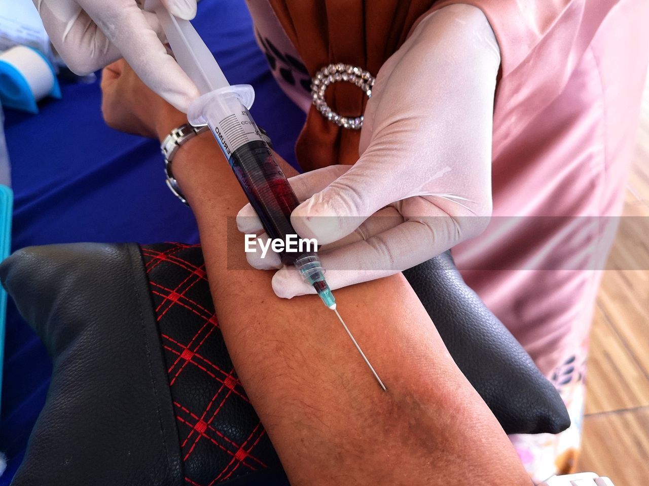 Midsection of doctor removing blood through injection in clinic