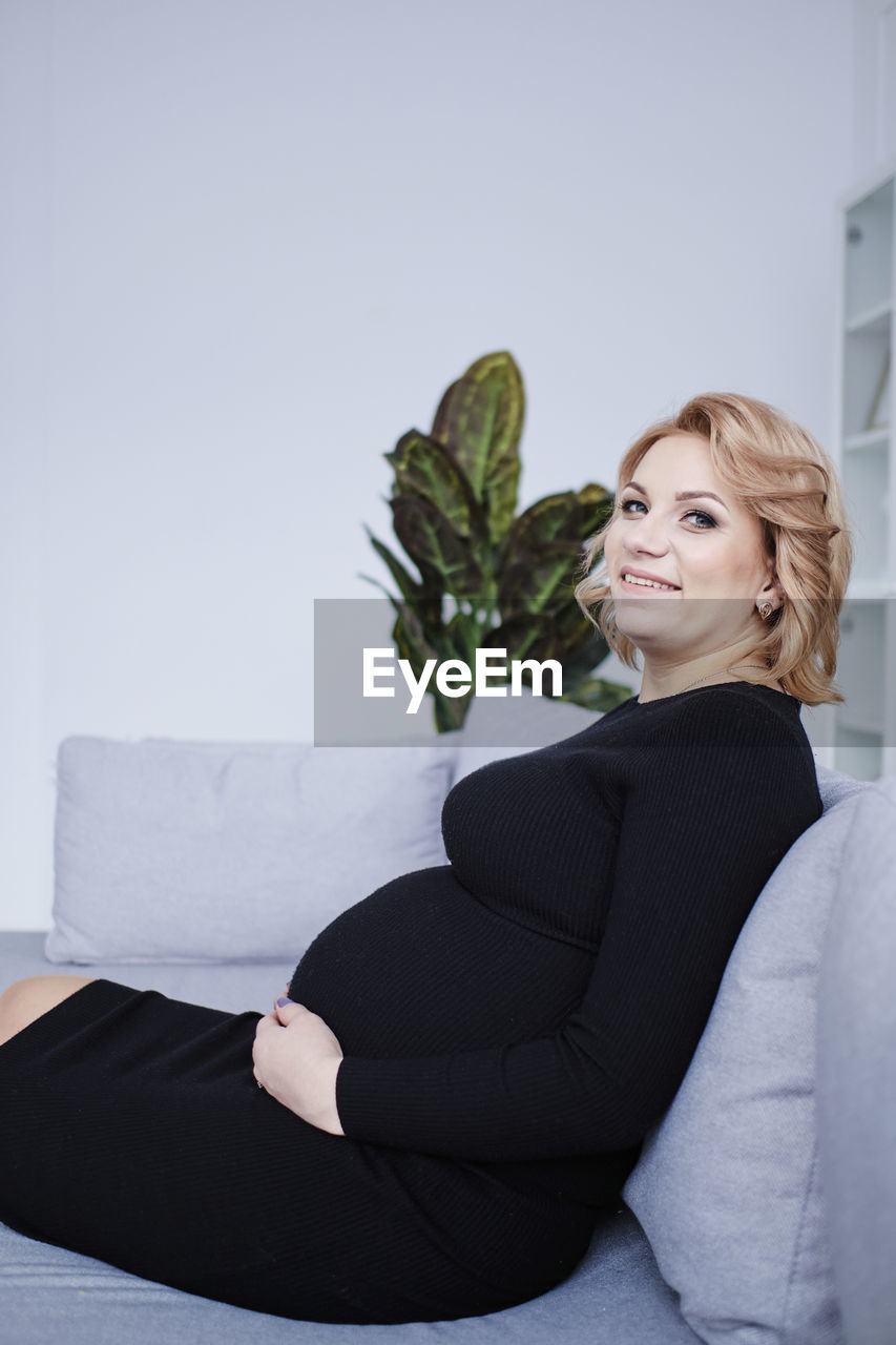 Pregnant woman in black dress smiling touching tummy