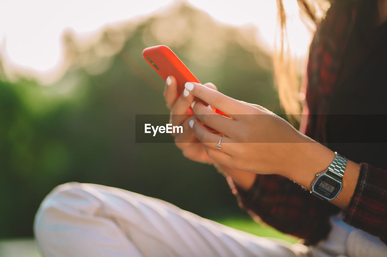 Midsection of woman using smart phone while sitting outdoors