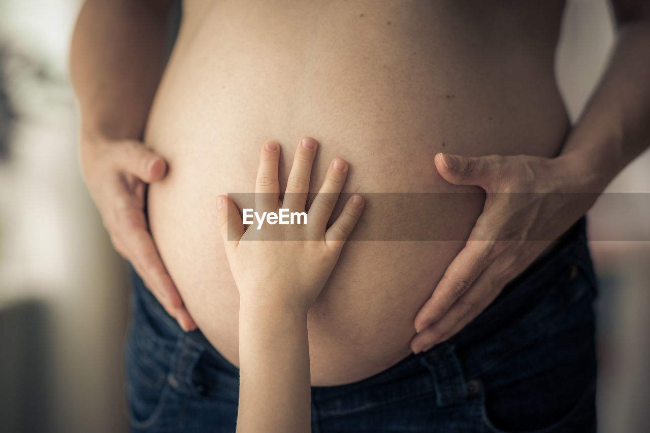 Big sisters hand touches pregnant mams belly