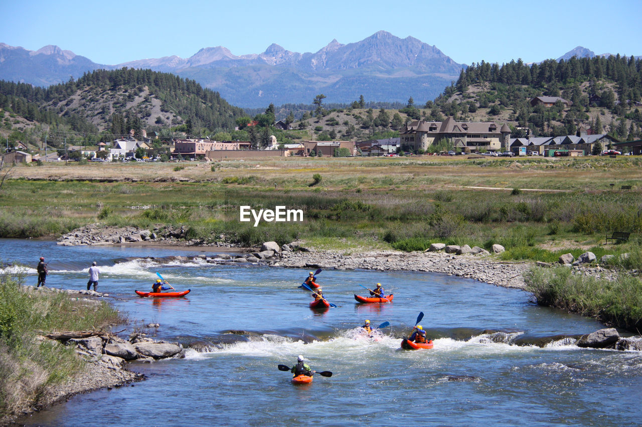 People kayaking on river against field