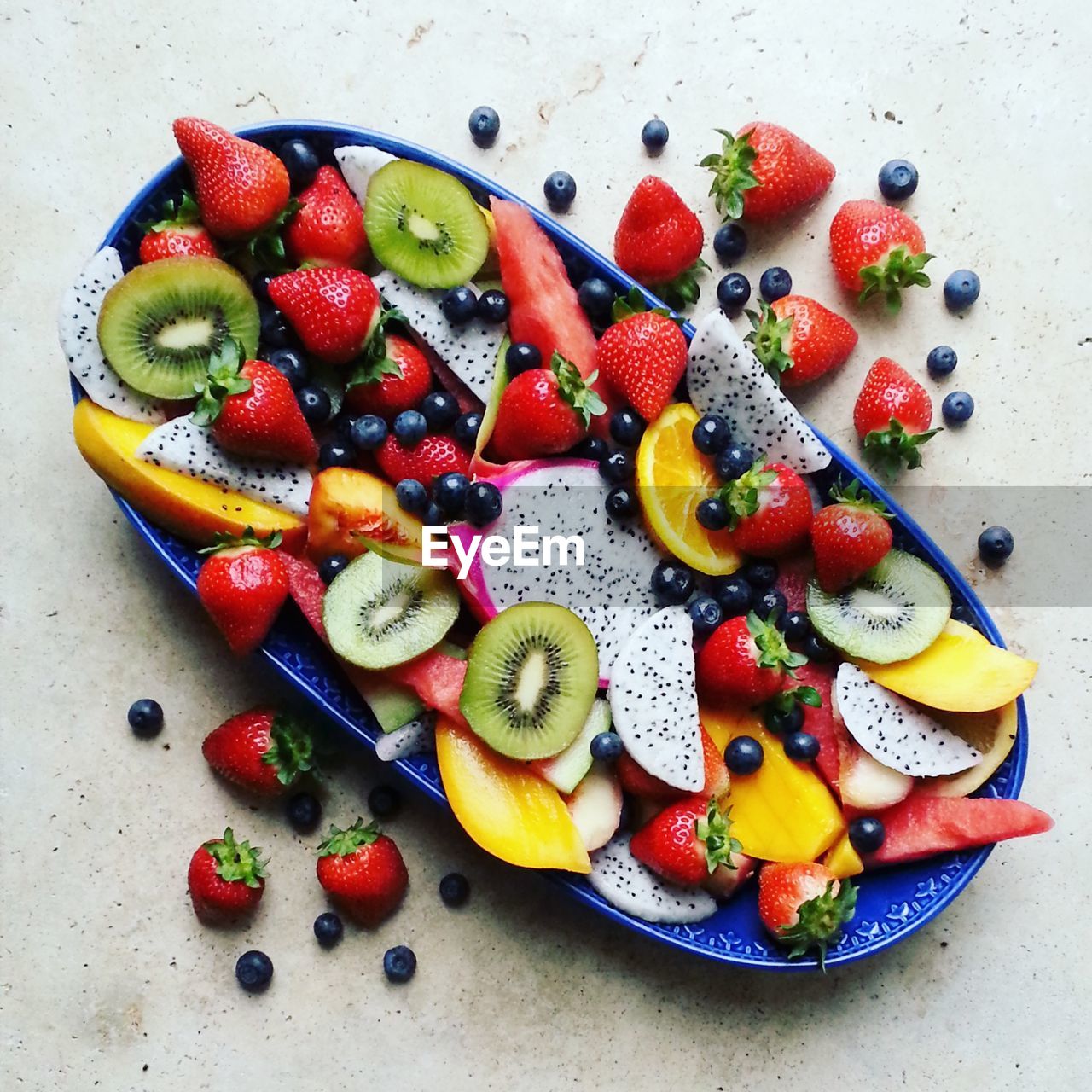 High angle view of colorful  tropical fruits in blue plate on stone table