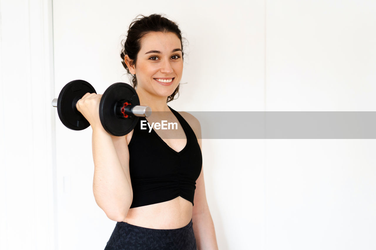 portrait of young woman exercising with dumbbells against white background