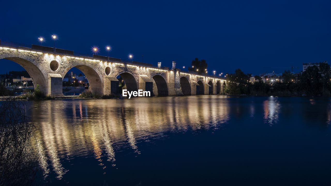 Illuminated bridge over water in city at night