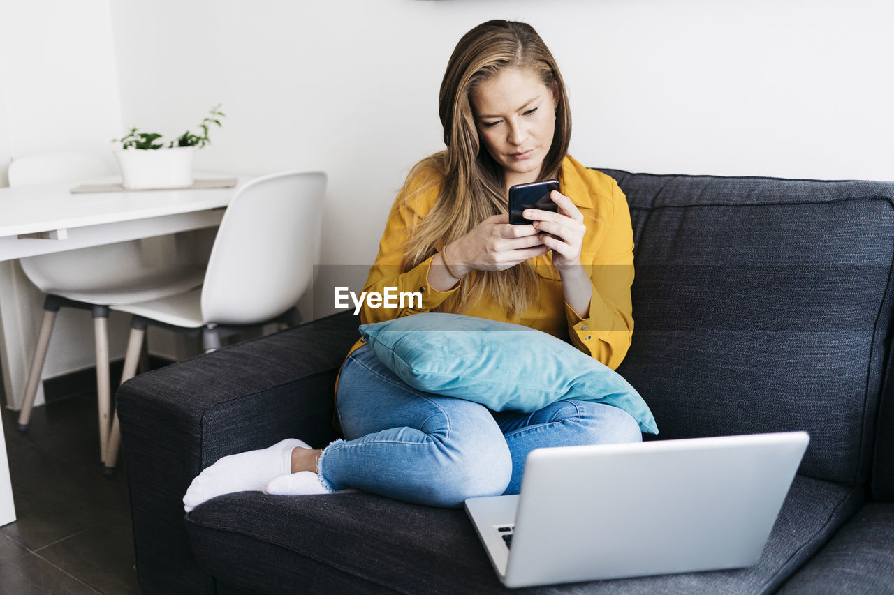 Young woman using mobile phone while sitting on sofa at home