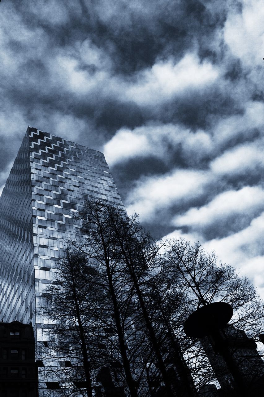 Low angle view of silhouette bare trees and modern buildings against cloudy sky