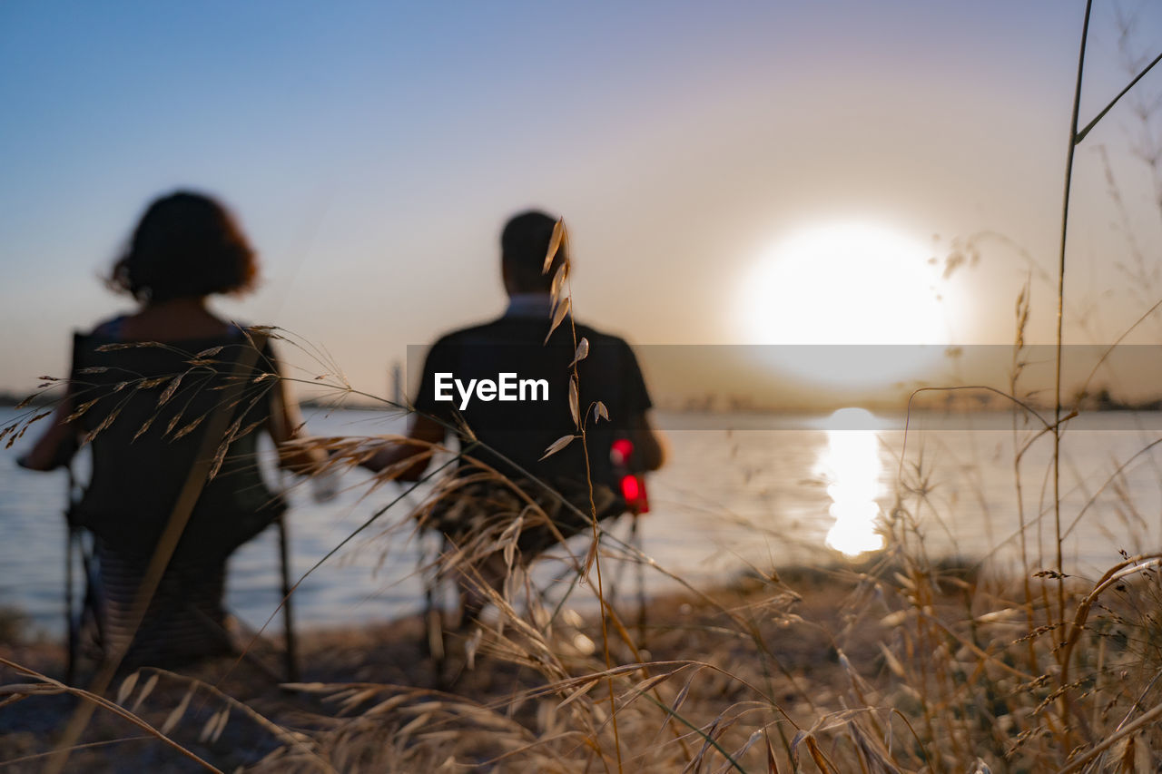 Rear view of people sitting at beach during sunset