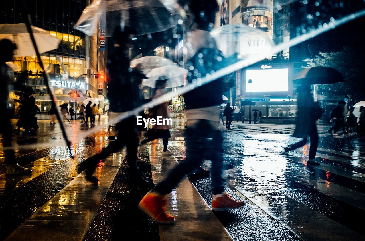 Blurred motion of people walking on wet street at night