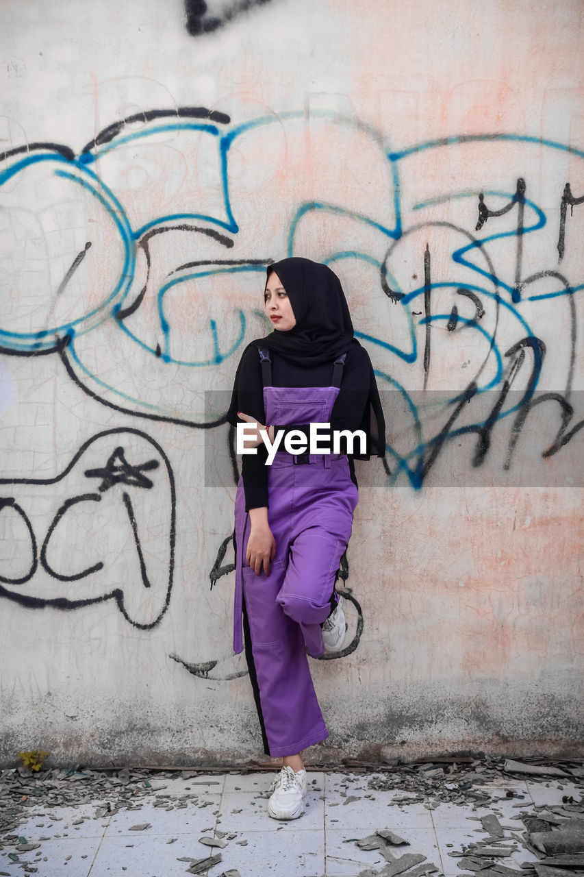 Full length of young woman standing against graffiti wall