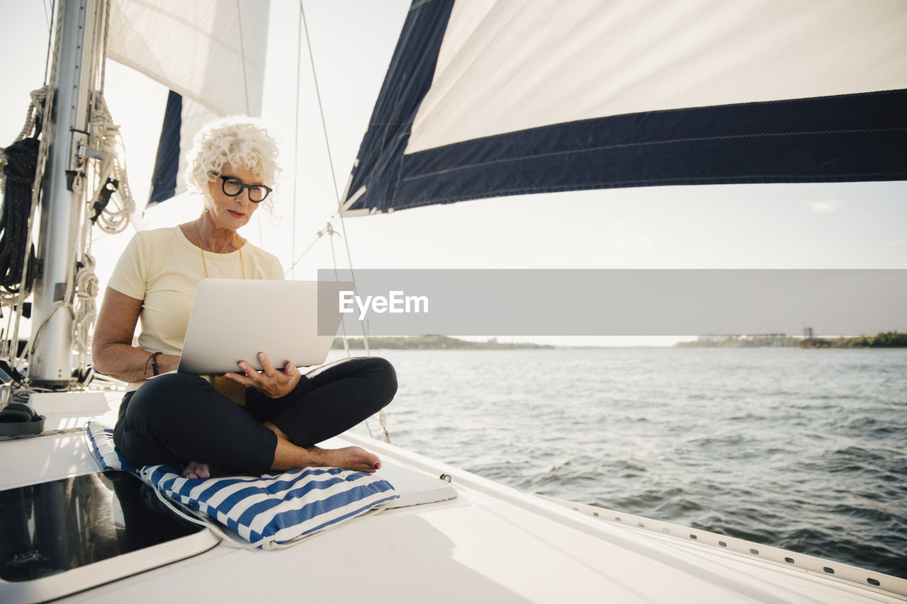 Senior woman working remotely while sailing boat on sunny day