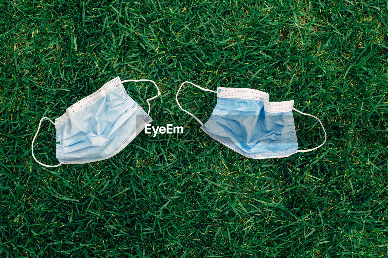 Two used sanitary masks lying on grass ground. disposable recyclable face mask flat lay. 