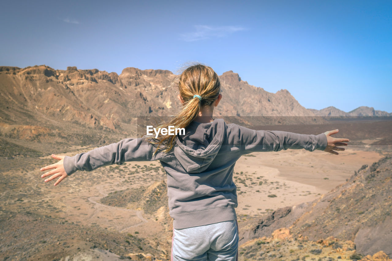 Rear view of girl with arms outstretched standing at desert