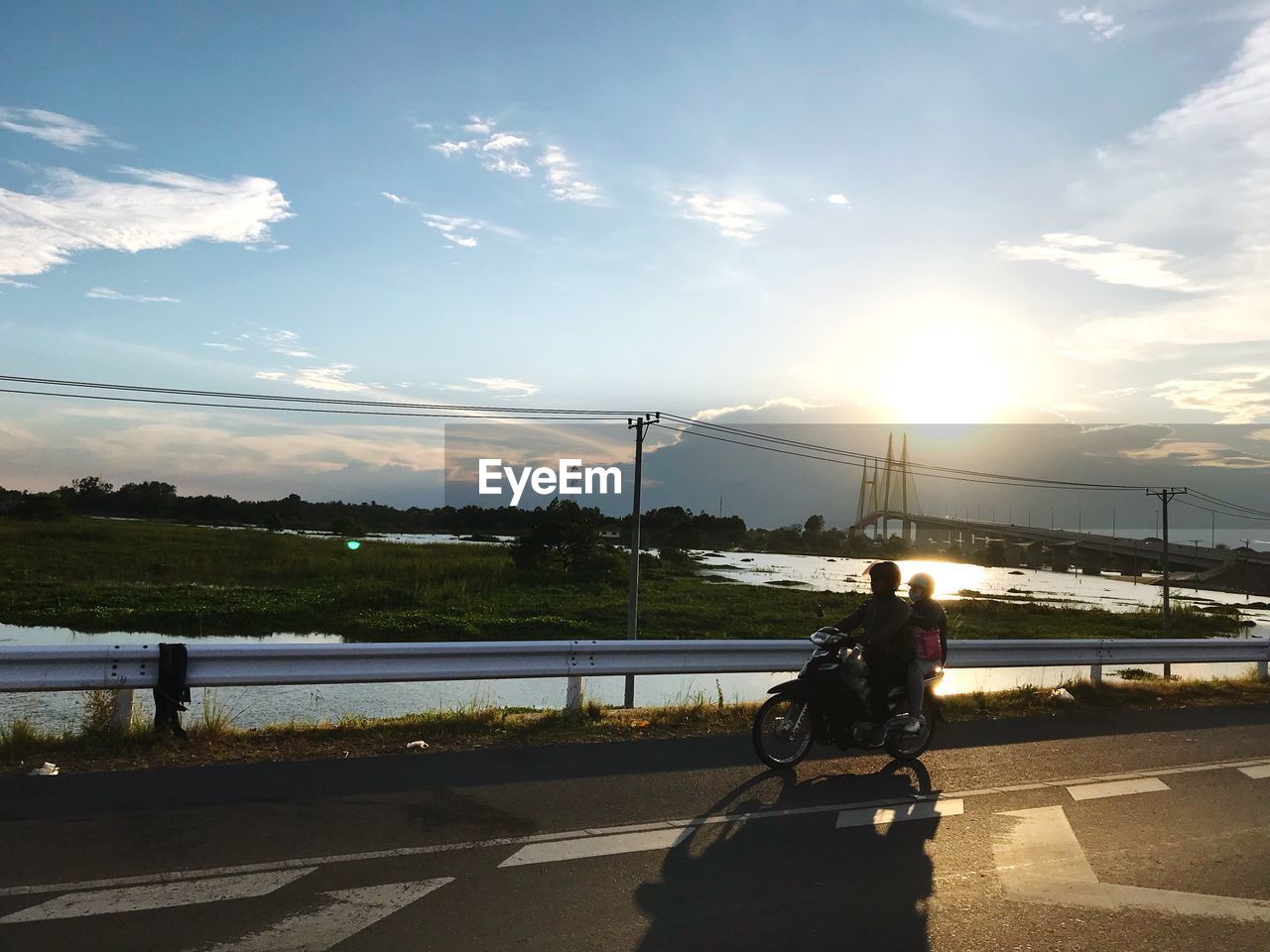 MAN ON BICYCLE BY RIVER AGAINST SKY
