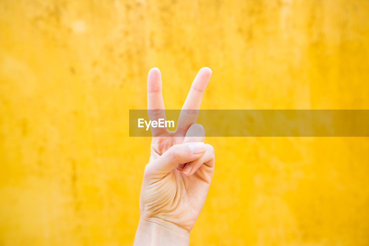 Cropped hand showing peace sign against yellow wall