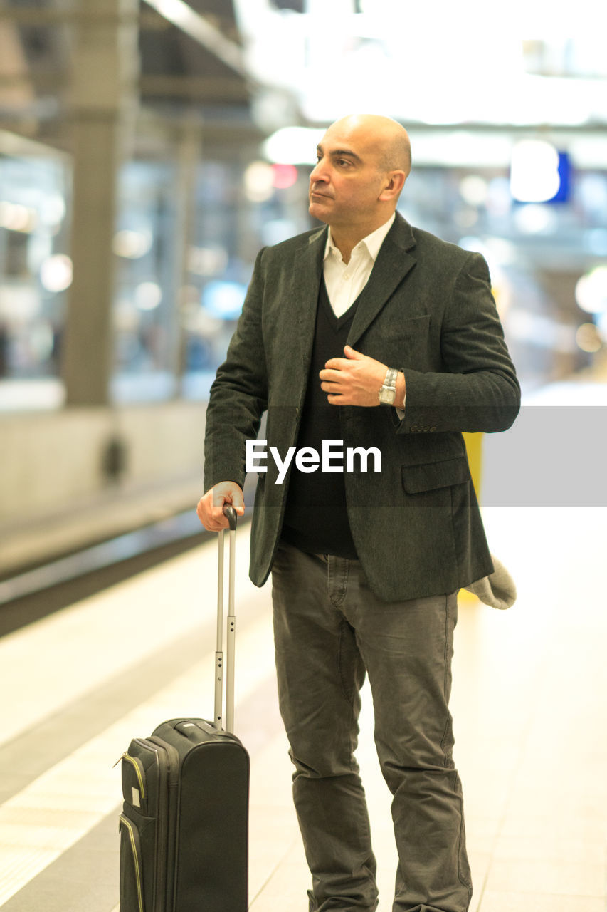 Mature man with suitcase standing at railroad station platform