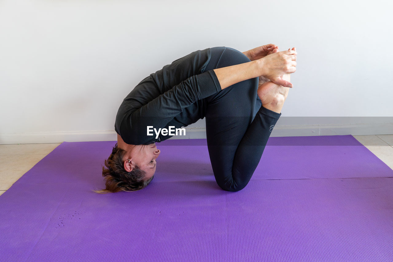 A woman practicing yoga on a purple mat on the floor
