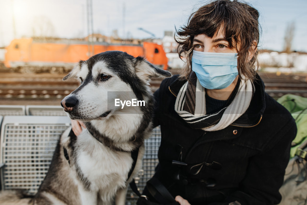 Woman wearing mask sitting with dog outdoors