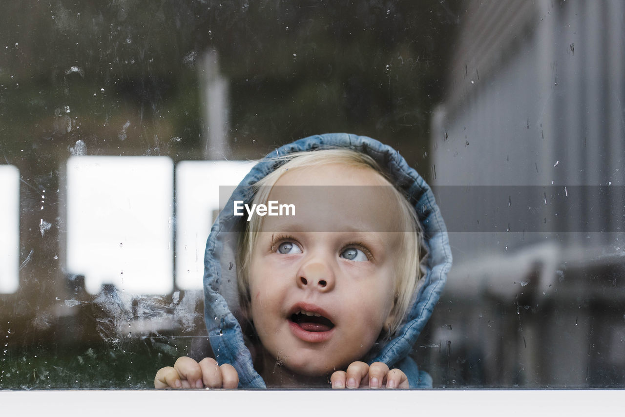 Close-up of girl looking through window seen through glass